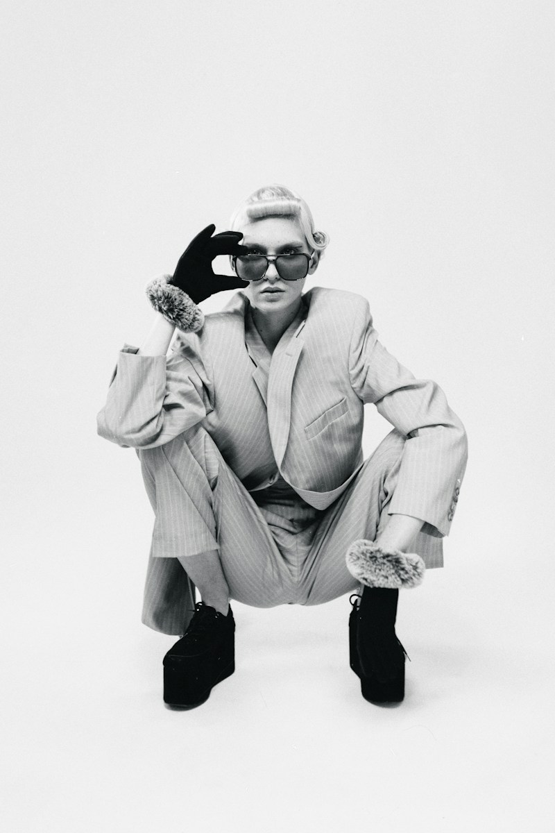 A person in a pinstripe suit and platform shoes crouching against a plain background